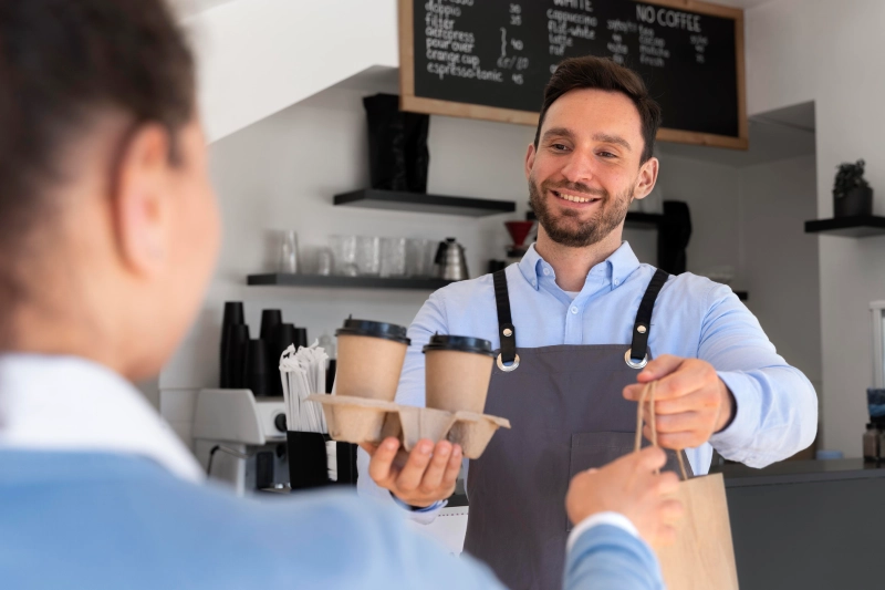 Image of a happy barista serving takeaway coffee and food to a customer, showcasing good service for a small business.