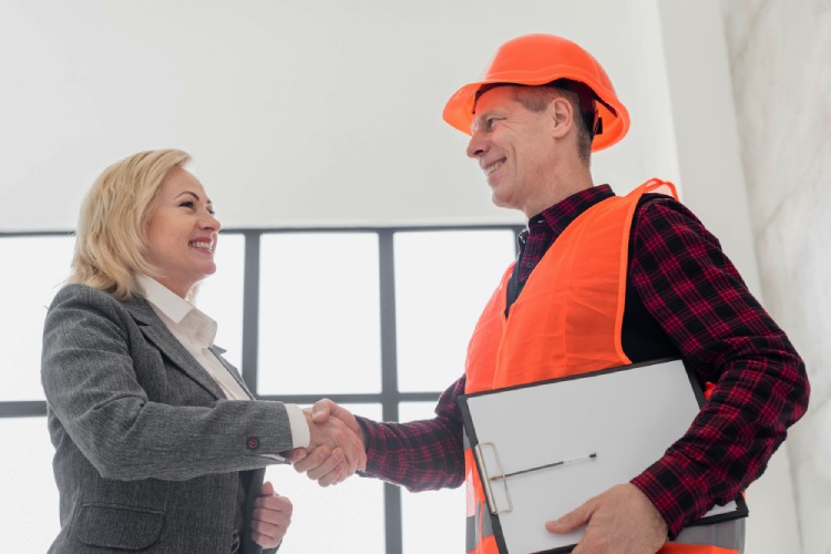 A construction manager in an orange hard hat shaking hands with a client.